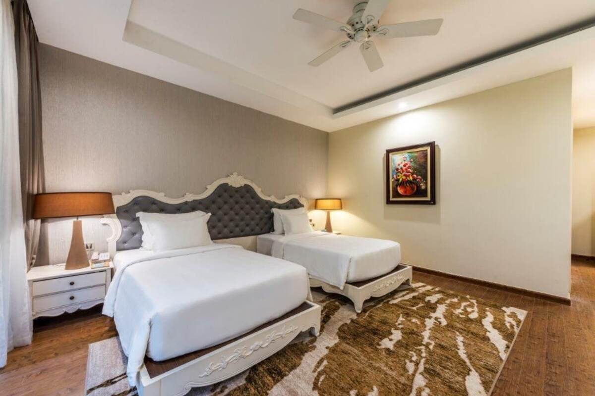 A hotel room with a large bed, two bedside tables, a ceiling fan, and a rug.