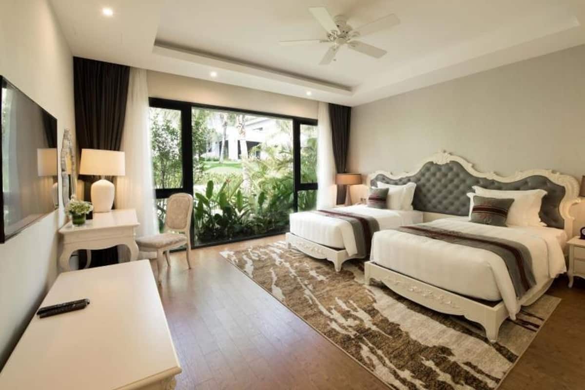 A hotel room with a bed, bedside tables, a desk, a chair, a ceiling fan, and a view of greenery outside.
