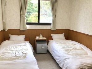 A hotel room with two beds, a small bedside table with a lamp, a heater, and a window with curtains. - Pension Lanpou (Fujikawaguchiko)