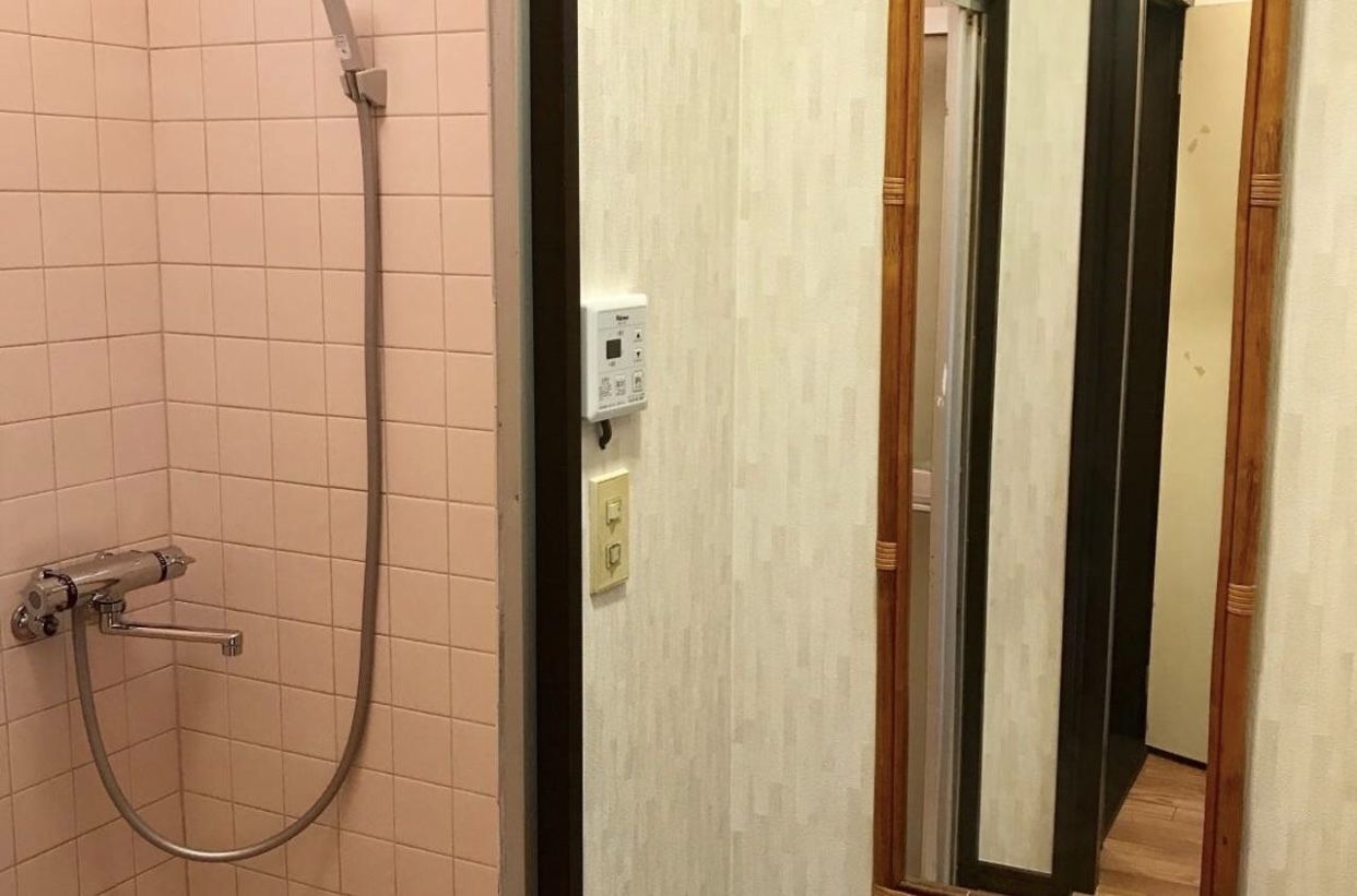 A shower area with a handheld showerhead and a wall-mounted control panel.