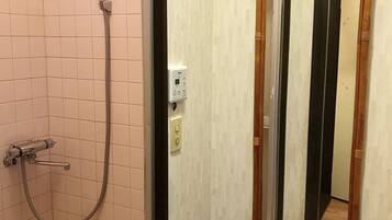 A shower area with a handheld showerhead and a wall-mounted control panel.