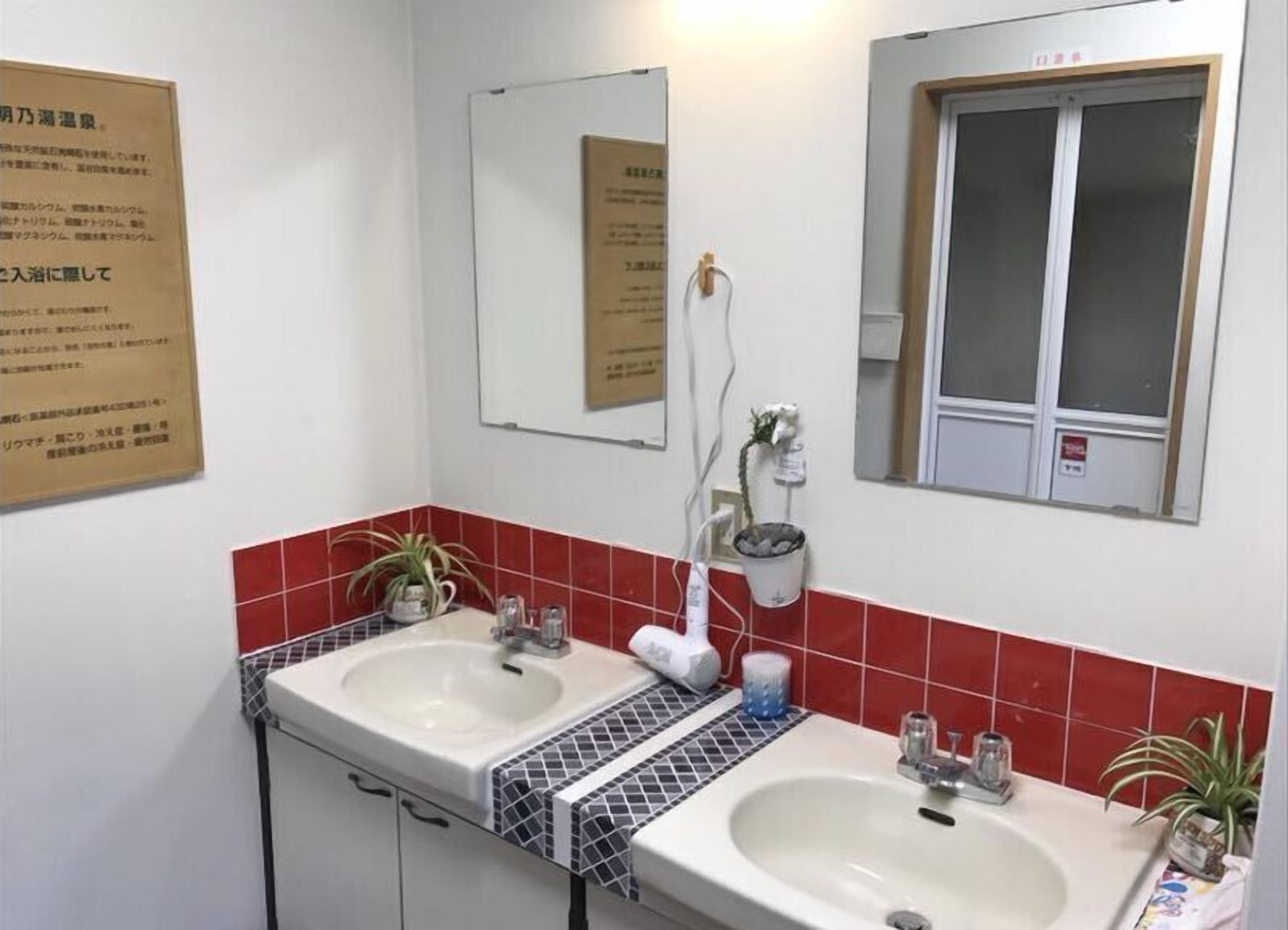 Une salle de bain avec deux lavabos, un miroir, une fenêtre et une plante en pot.