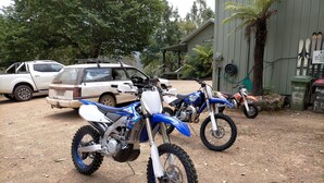 Two dirt bikes parked on a gravel surface with a white car and a building in the background. - Riverbend Homestead Horse and Farmstay (Freeburgh)