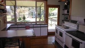 A kitchen with a large window, wooden cabinets, a stove, and a sink. - Riverbend Homestead Horse and Farmstay (Freeburgh)