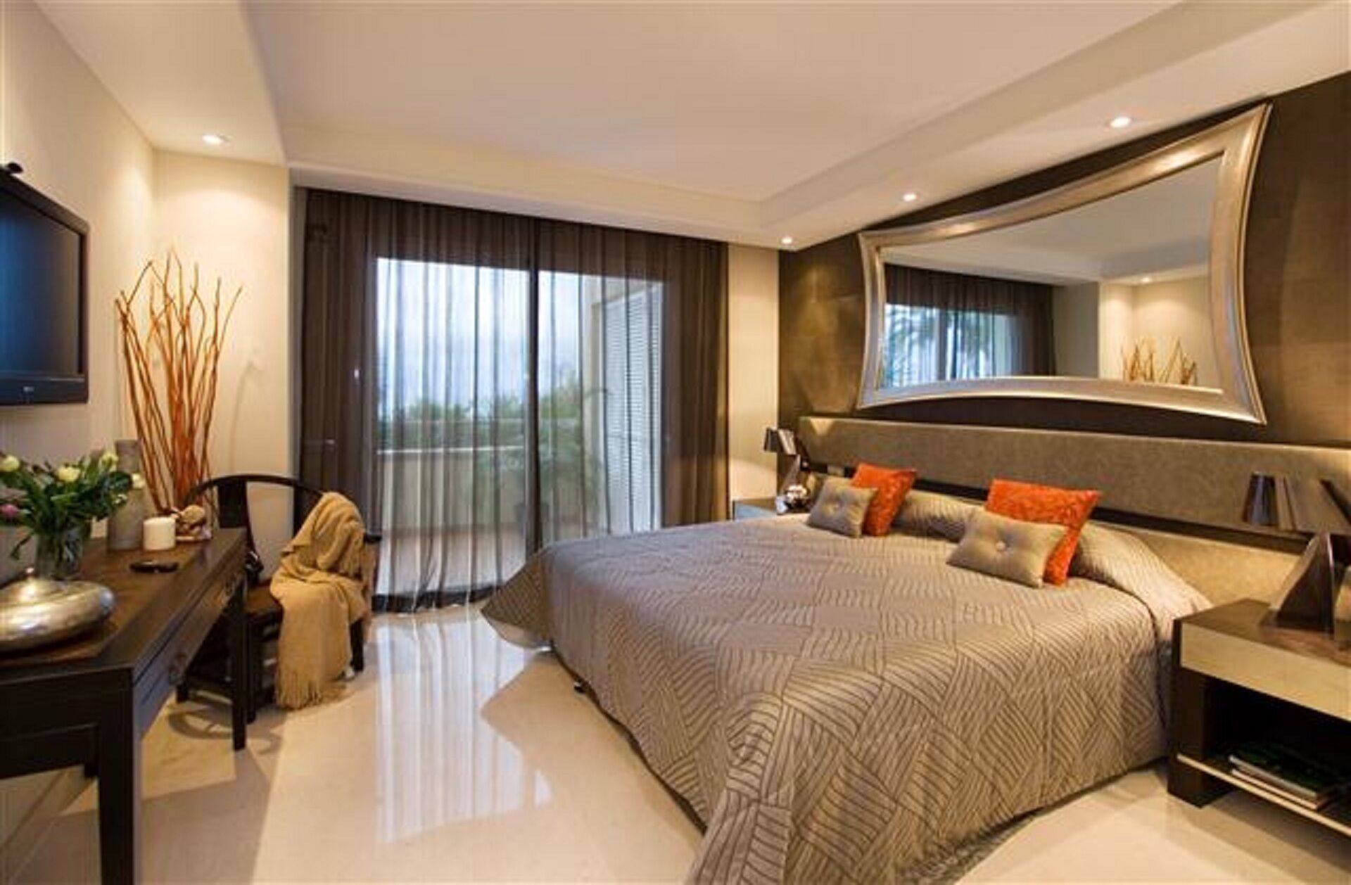 A modern bedroom with a large bed, a desk, and a large mirror.