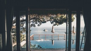 Een open deur die leidt naar een balkon met uitzicht op zee, een standbeeld en een hanglamp.