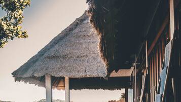 A pool area with a thatched roof, wooden deck, and a view of the hills.