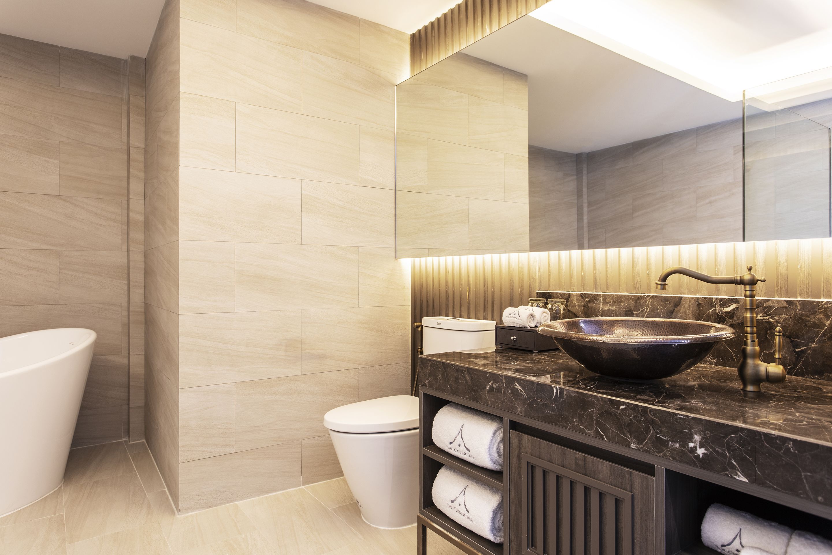 A modern bathroom with a large mirror, a vessel sink, a toilet, and a bathtub.