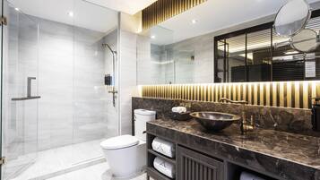 Een moderne badkamer met een douchecabine van glas, een wit toilet, een grote spiegel en een marmeren aanrecht met een wastafel.