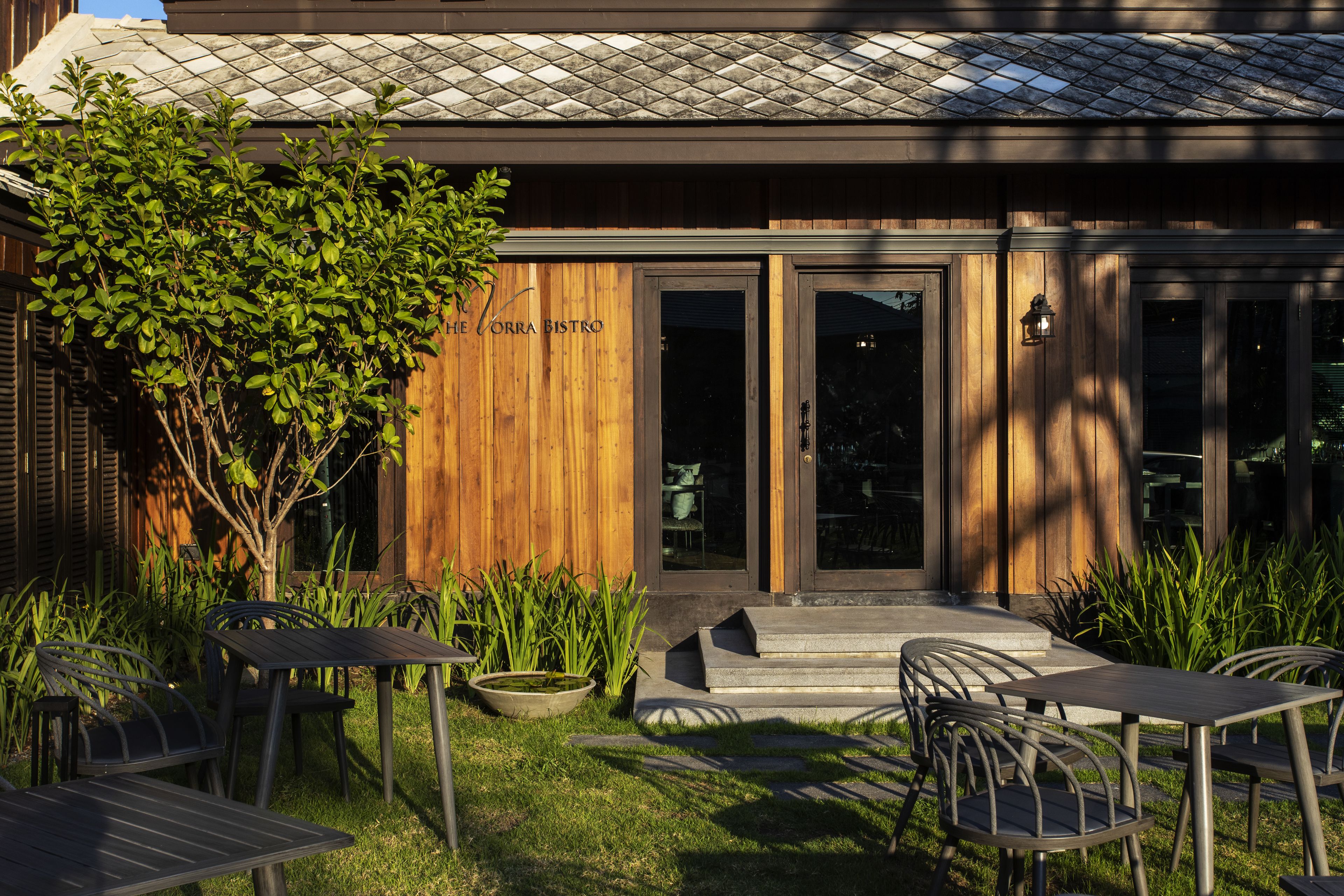 Un espace extérieur aménagé avec des tables et des chaises, un bâtiment en bois sur lequel on peut lire l’inscription « The Corra Bistro », et un petit arbre.