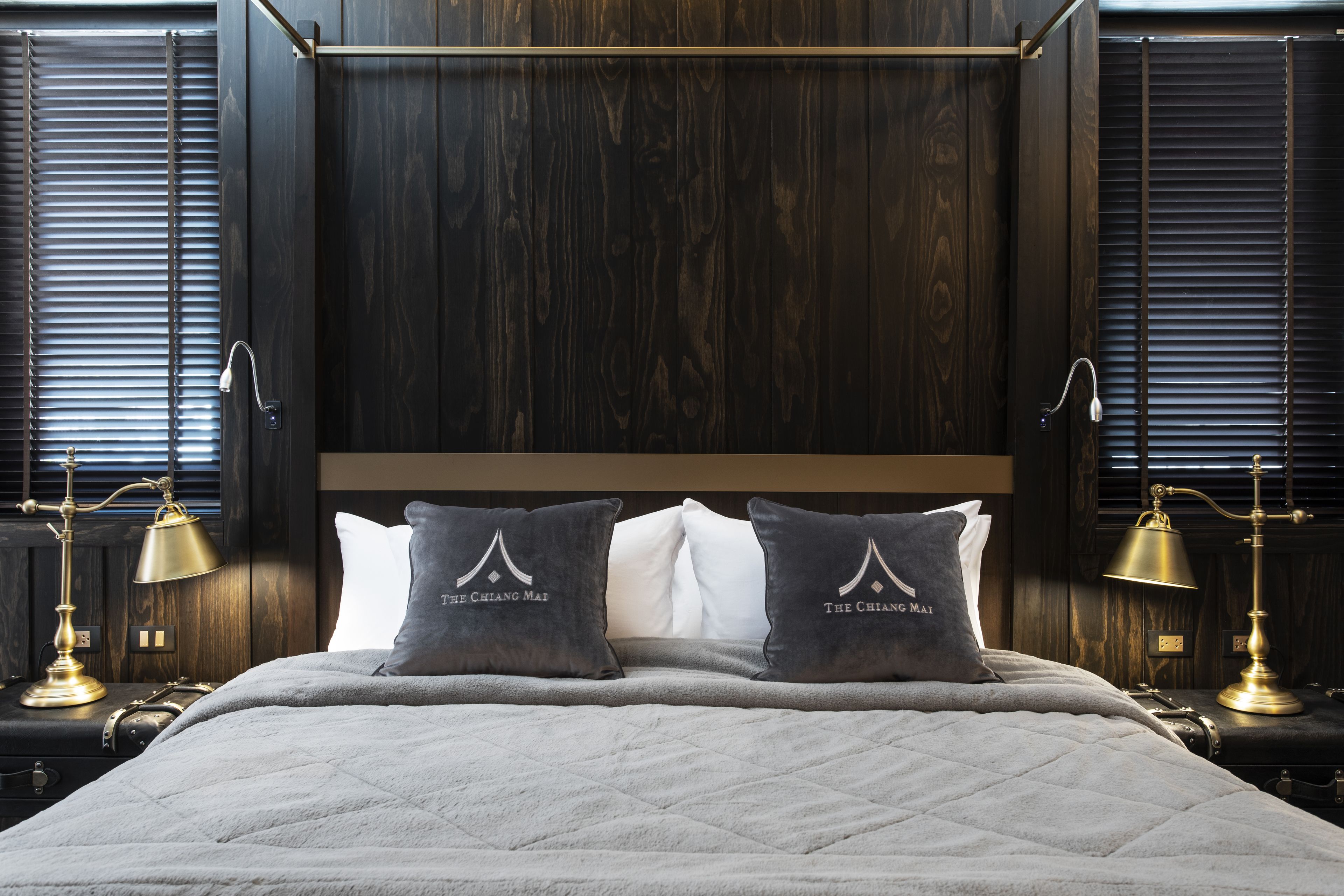 A neatly made bed with a quilted cover, two pillows with text, and two bedside lamps.