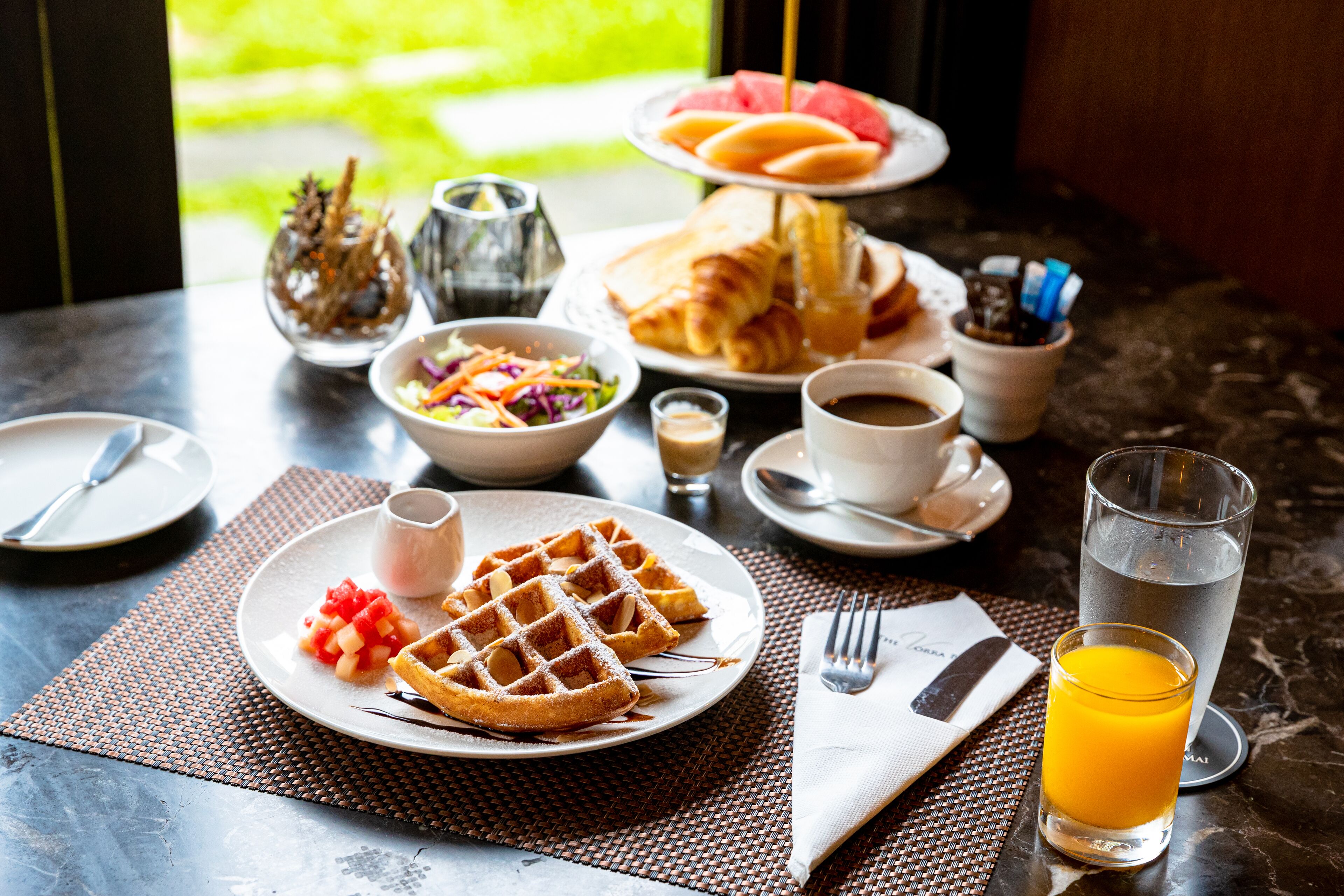 A breakfast setting with waffles, a glass of orange juice, and a variety of other breakfast items on a table.