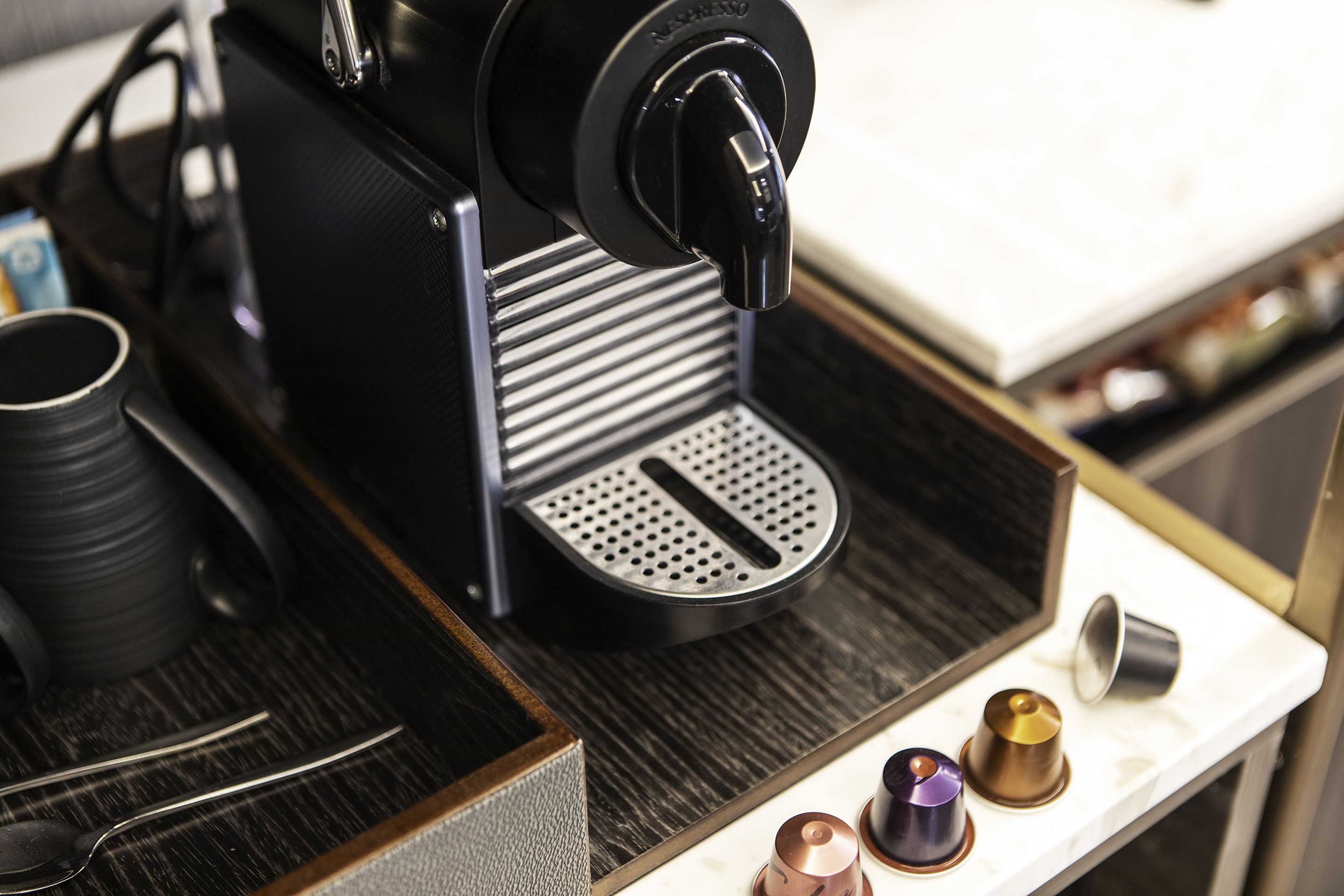 A coffee machine with a drip tray, a cup, and a spoon on a wooden surface.