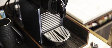 Une machine à café avec un bac de récupération, une tasse et une cuillère, le tout posé sur une surface en bois.