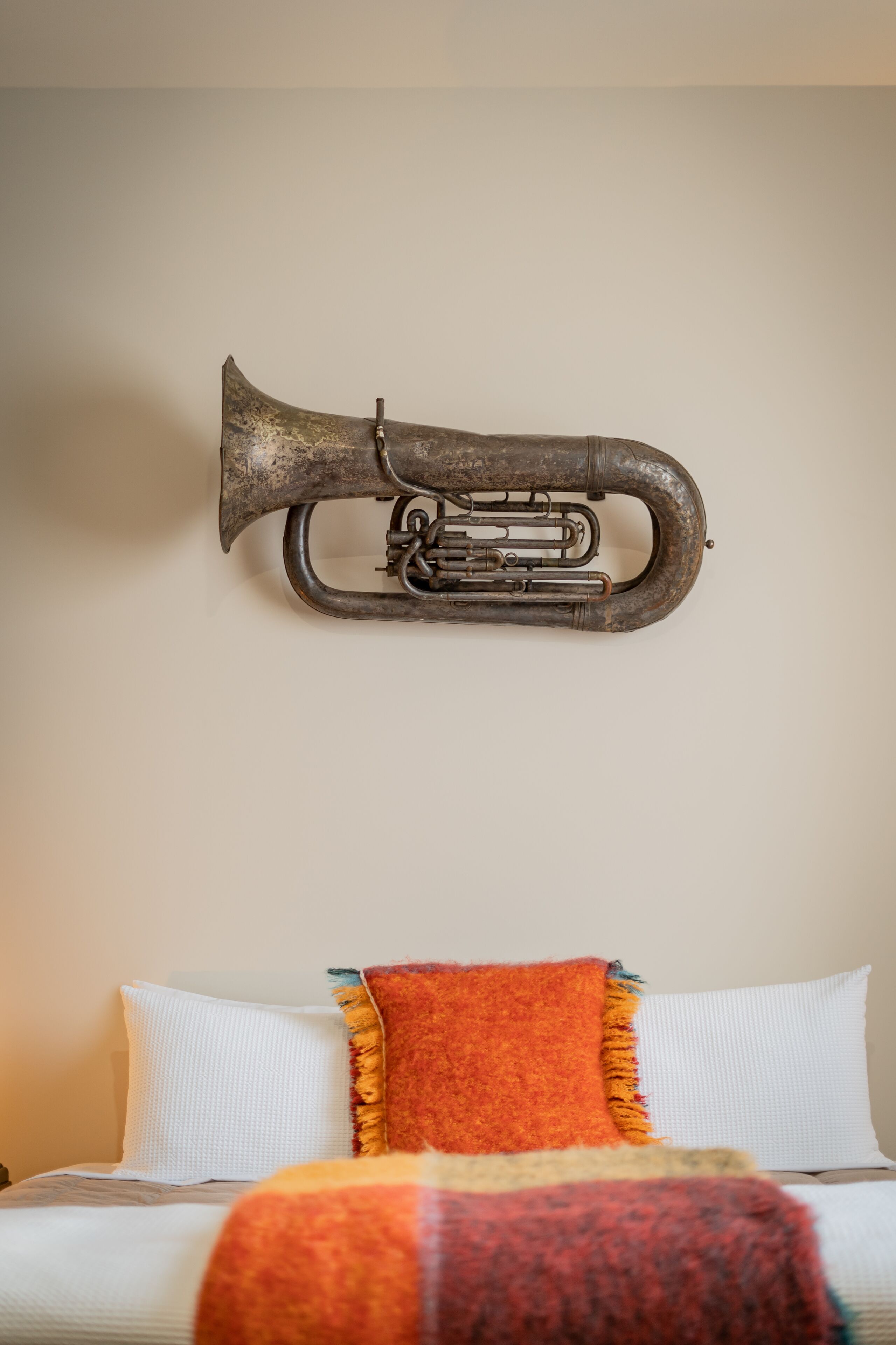A bed with white and multicolored pillows, a brass trumpet mounted on the wall, and a plain wall.