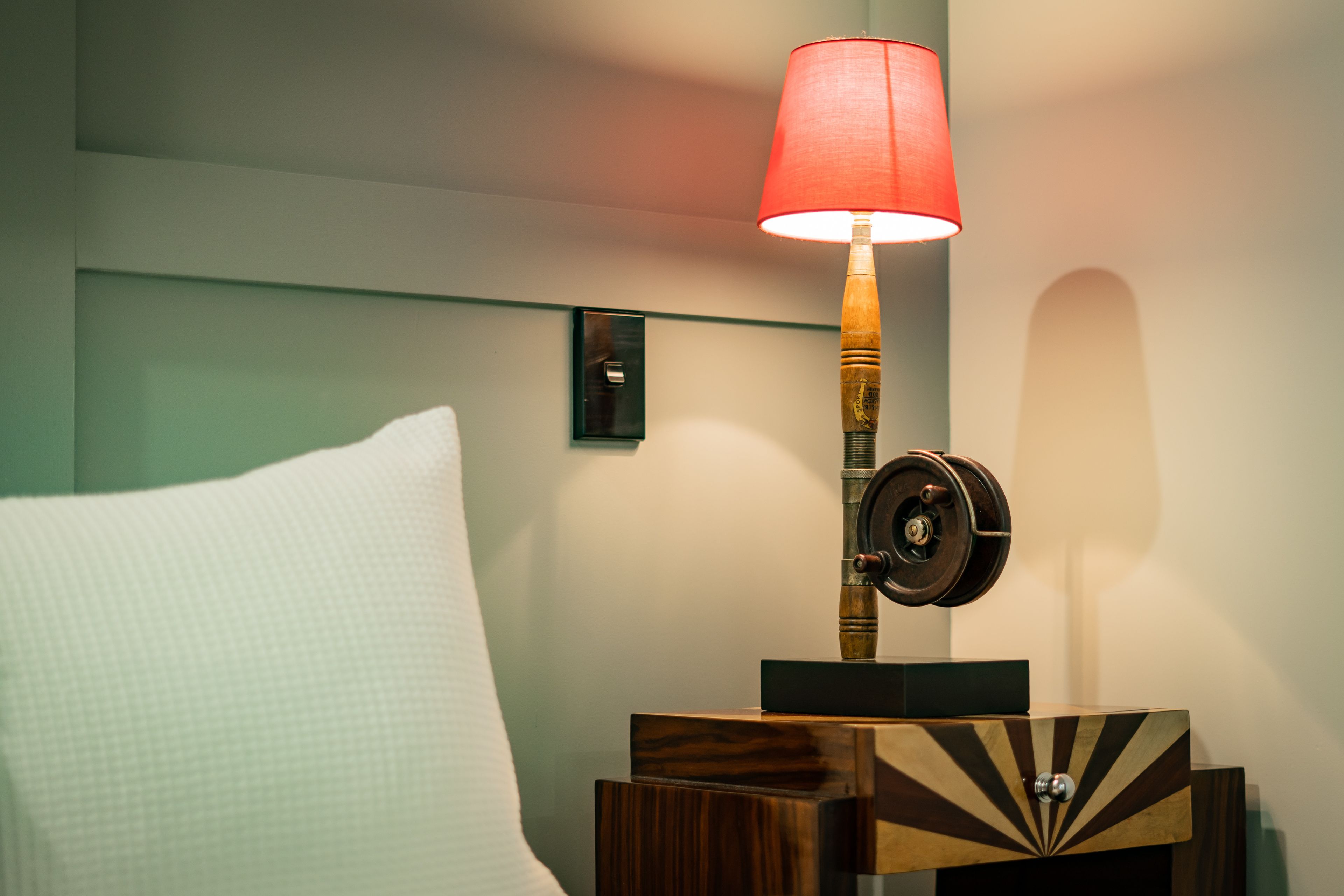 A neatly made bed with a white pillow and a wooden nightstand with a lamp.