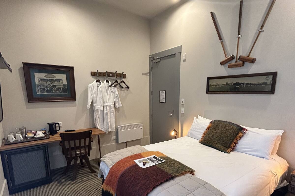 A hotel room with a bed, a desk with a chair, a small kitchenette, and a door.