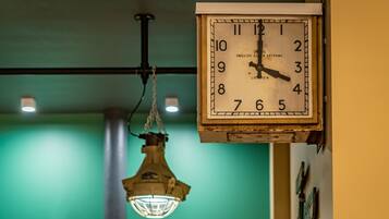 Un reloj de pared con diseño clásico, una lámpara colgante de estilo industrial y una pared verde al fondo.