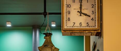 A wall-mounted clock with a classic design, a hanging industrial-style light fixture, and a green wall in the background.