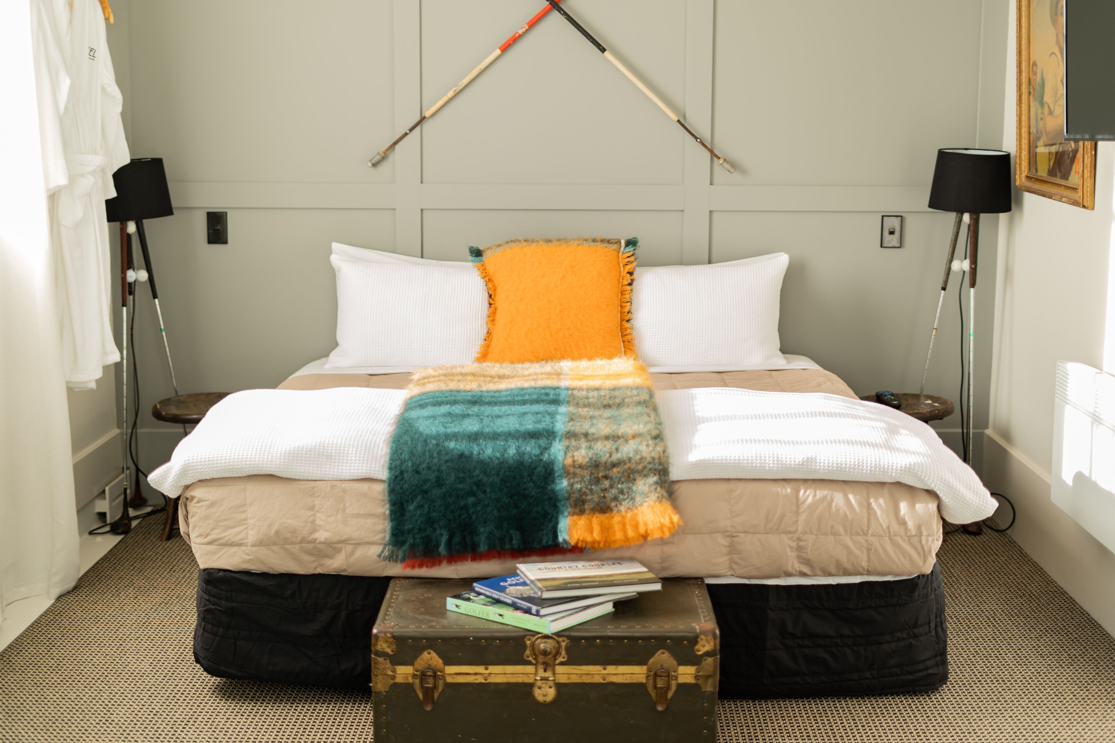 A neatly made bed with a colorful blanket, a bedside table with books, and a suitcase on the floor.