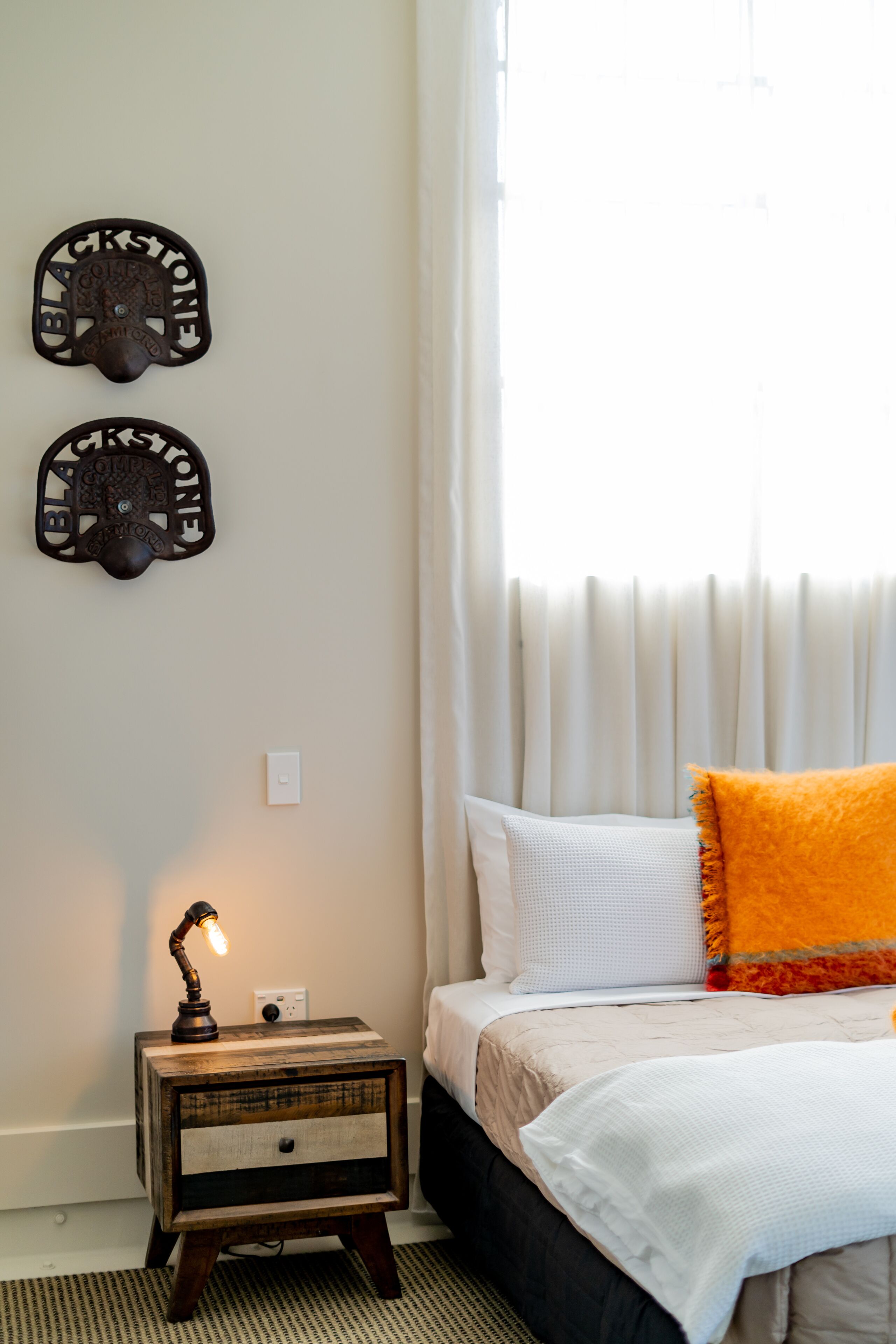 A bedroom with a bed, a nightstand with a lamp, and two wall-mounted clocks.