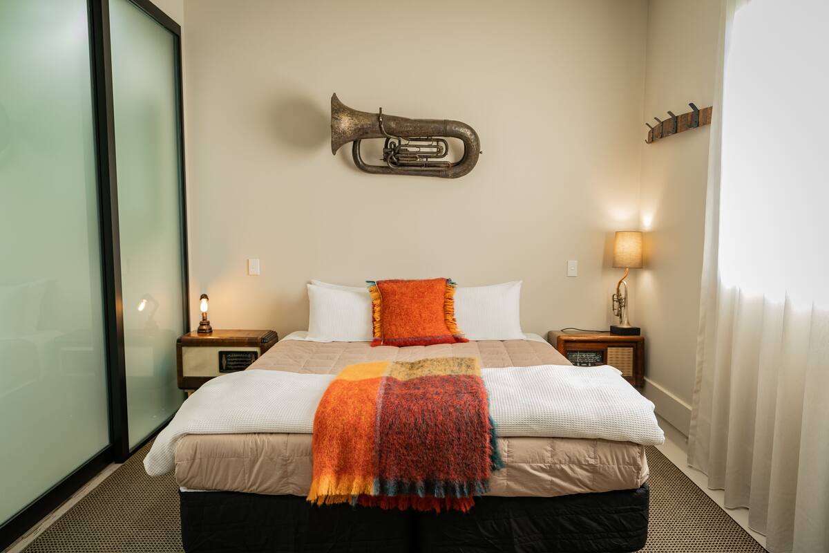 A hotel room with a bed, a wall-mounted trumpet, a lamp, and a radio on a bedside table.