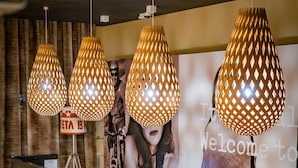 Ein Empfangstresen mit Glastischplatte, Holzfuß und drei Lampen mit geometrischem Muster.