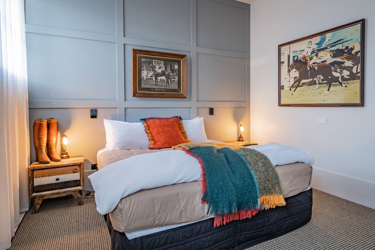 A neatly made bed with a white comforter and multiple pillows, a wooden nightstand with a lamp, and a framed picture on the wall.