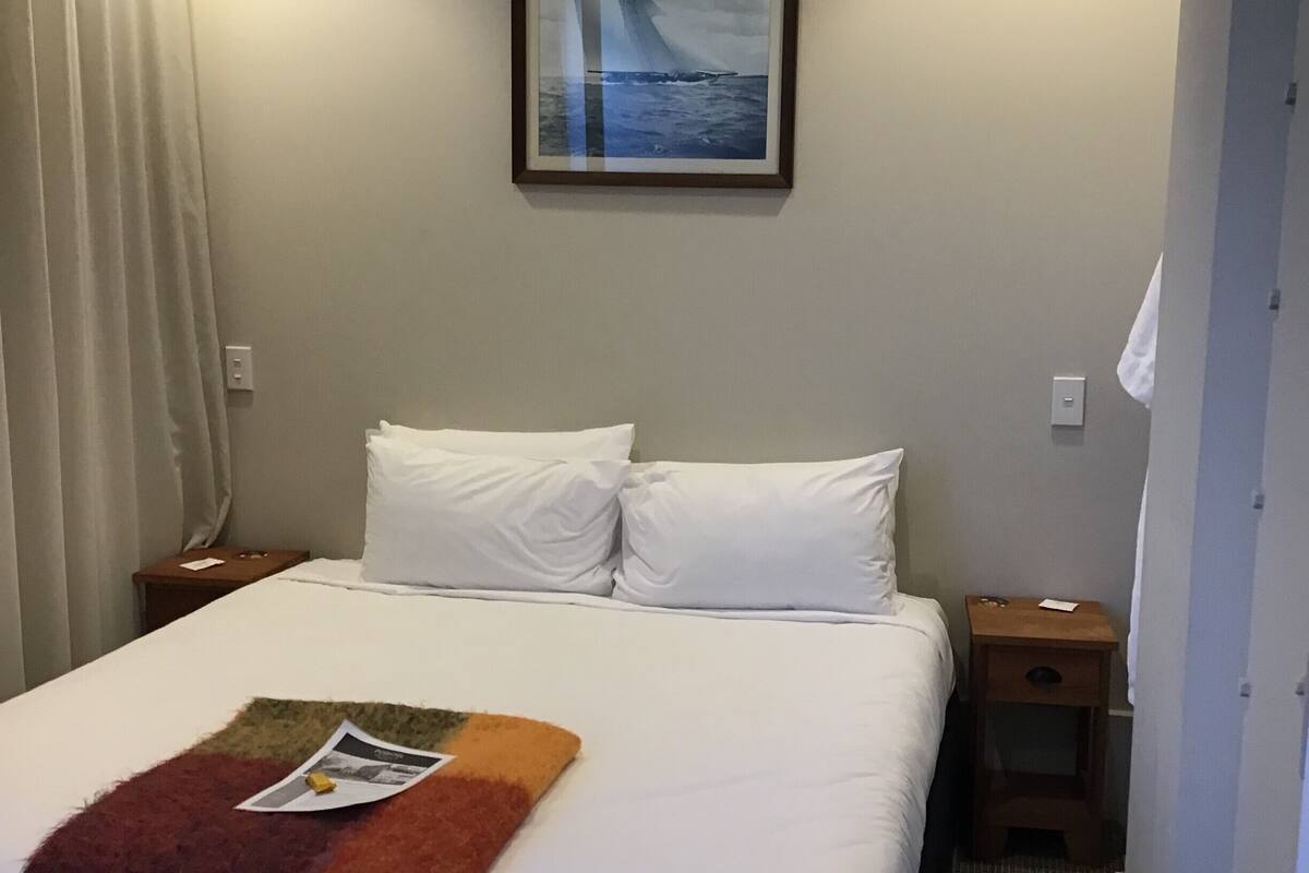 A hotel room with a bed, white linens, a framed picture on the wall, and two bedside lamps.