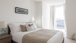 A neatly arranged bedroom with a large bed, a bedside table with a lamp, and a window with curtains. - A luxury, contemporary 2Bed & 2Bath Apartment Next to London Museum (London)