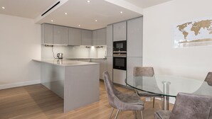 A modern kitchen with grey cabinets, a glass island, and a dining area with grey chairs. - A luxury, contemporary 2Bed & 2Bath Apartment Next to London Museum (London)