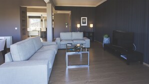 Een moderne woonkamer met een bank, salontafel en televisie. Achtergrond toont een eethoek met een tafel en stoelen.