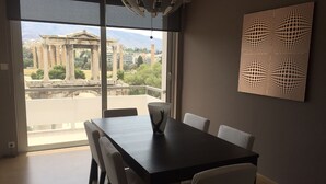 Een eethoek met uitzicht op oude Griekse architectuur, een moderne tafel en een behang met patroon.