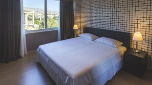 Hotelkamer met een groot bed, twee bedlampen, uitzicht op oude ruïnes door het raam en een behang met patroon.