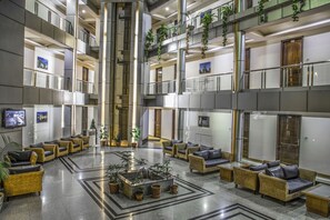 A multi-level hotel lobby with seating areas, a central water feature, and potted plants. - Sukhsagar Regency (Shimla)