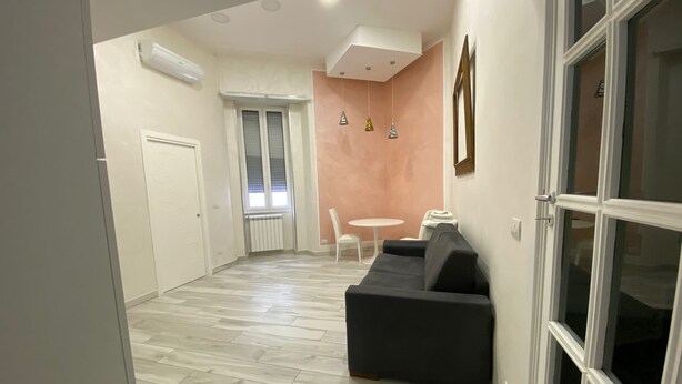Una sala de estar moderna con un sofá negro, una mesa blanca y una ventana con persianas.