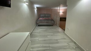 Un pasillo estrecho con una cama al final, suelo de baldosas e iluminación en la pared.