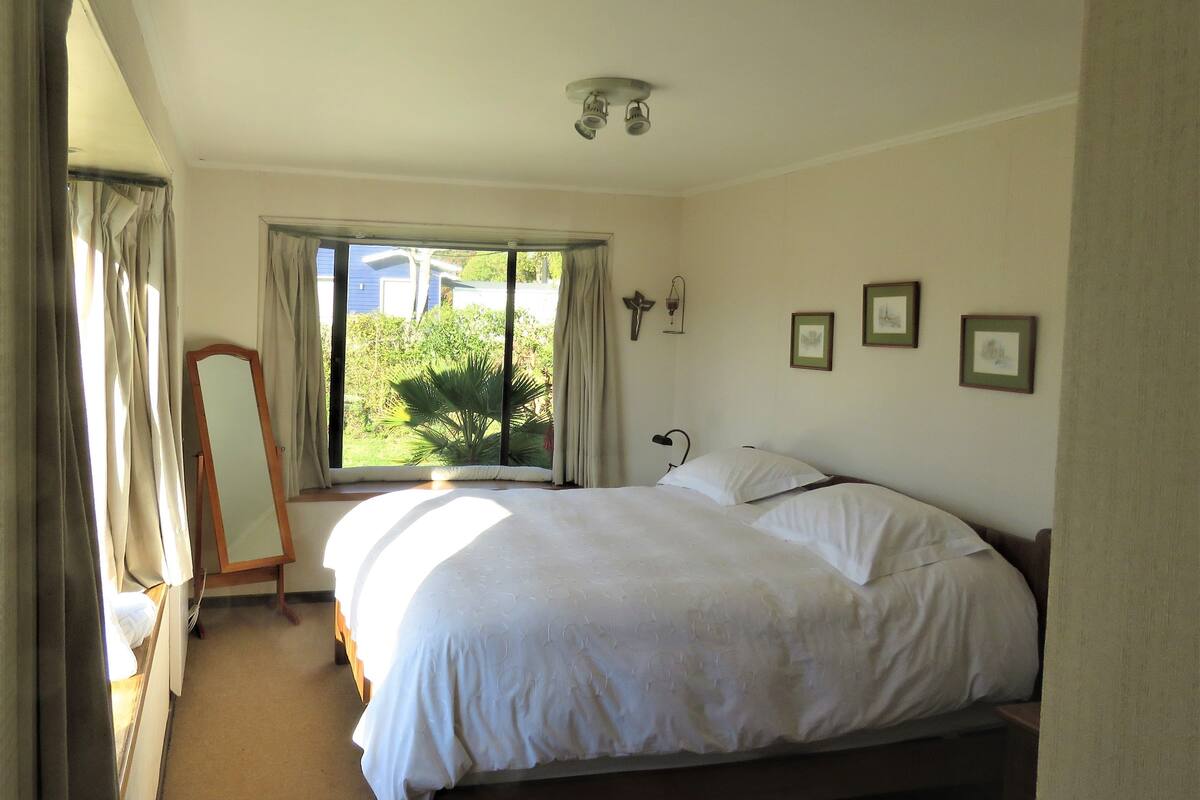 A bedroom with a bed, a window with curtains, a bedside table, and a mirror.