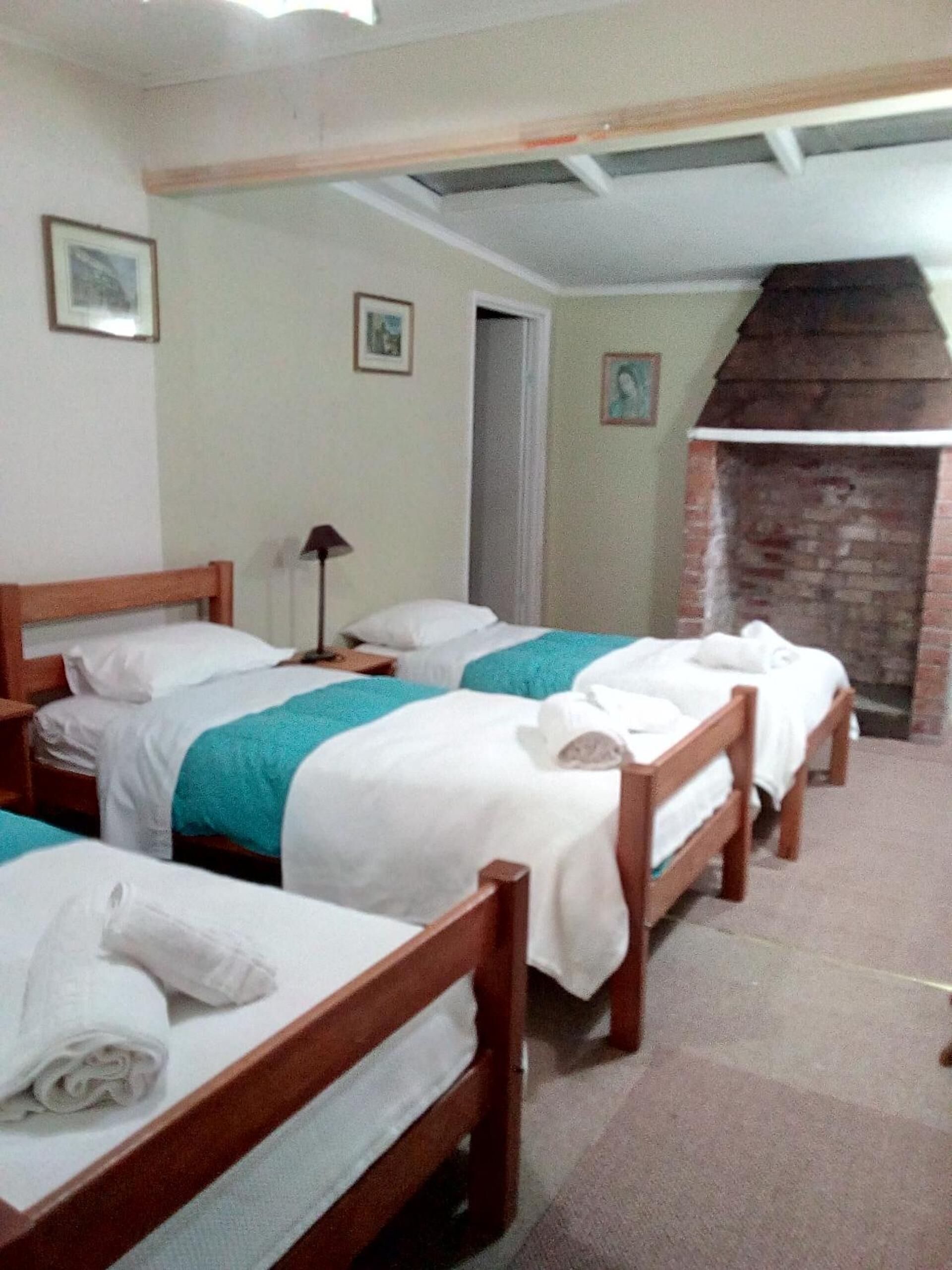 A room with four wooden beds, each with white linens and teal blankets. There is a brick fireplace and a door leading to another room.
