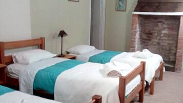 A room with four wooden beds, each with white linens and teal blankets. There is a brick fireplace and a door leading to another room.