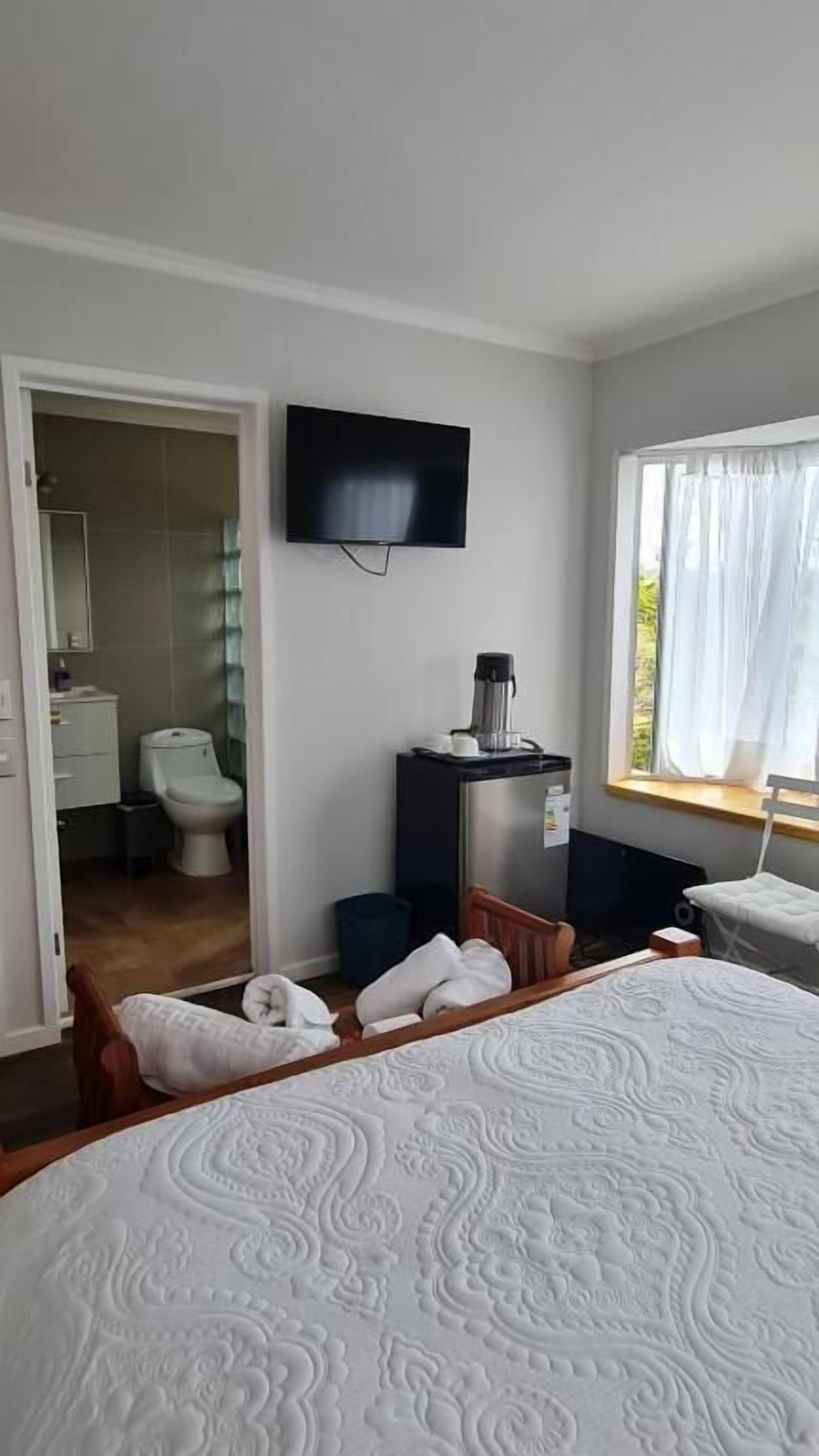 Una habitación de hotel con cama, televisor, ventana con cortinas, una mesita peque ña y una silla.