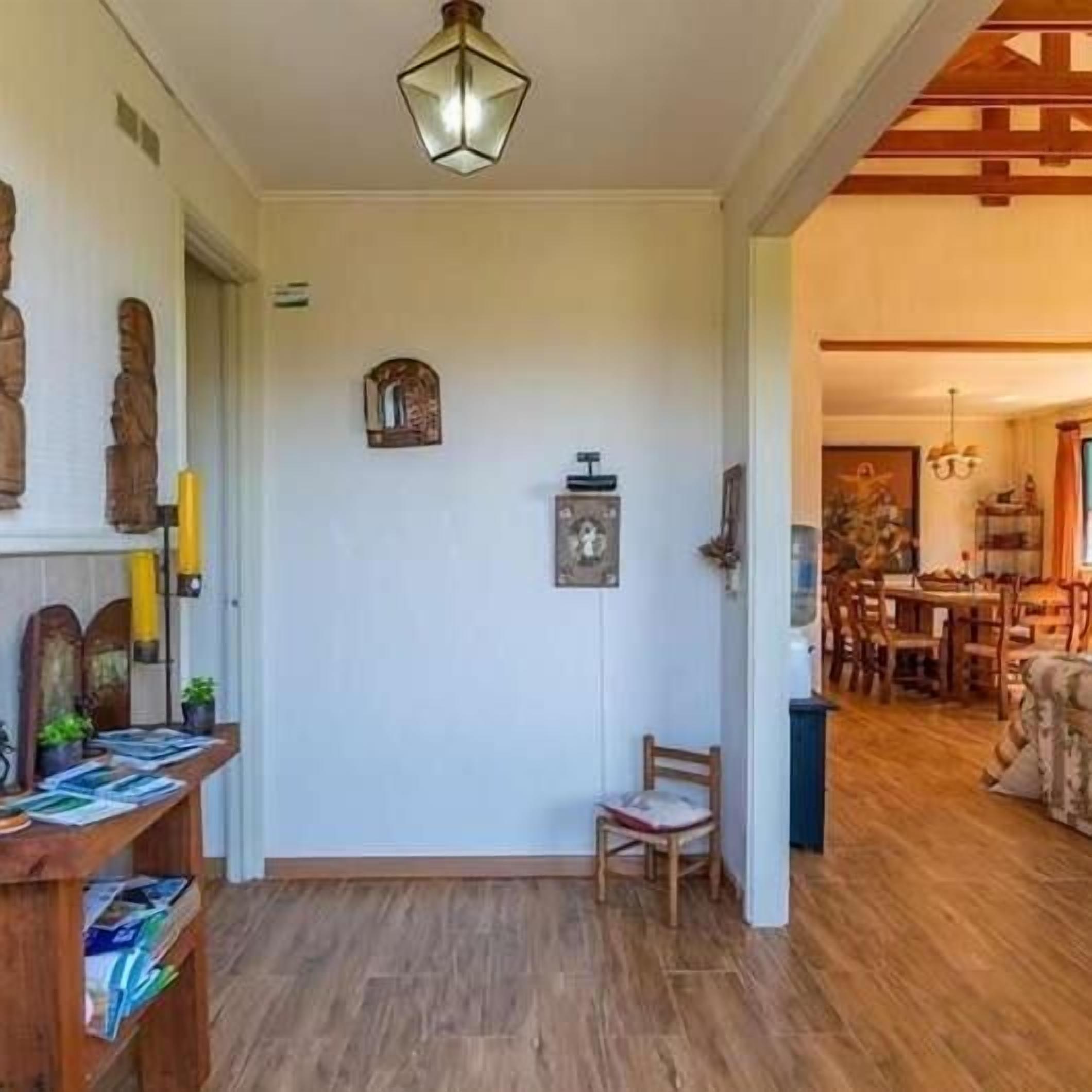 Una habitación con piso de madera, una mesa con sillas, una lámpara colgante y una puerta que da a otra habitación.