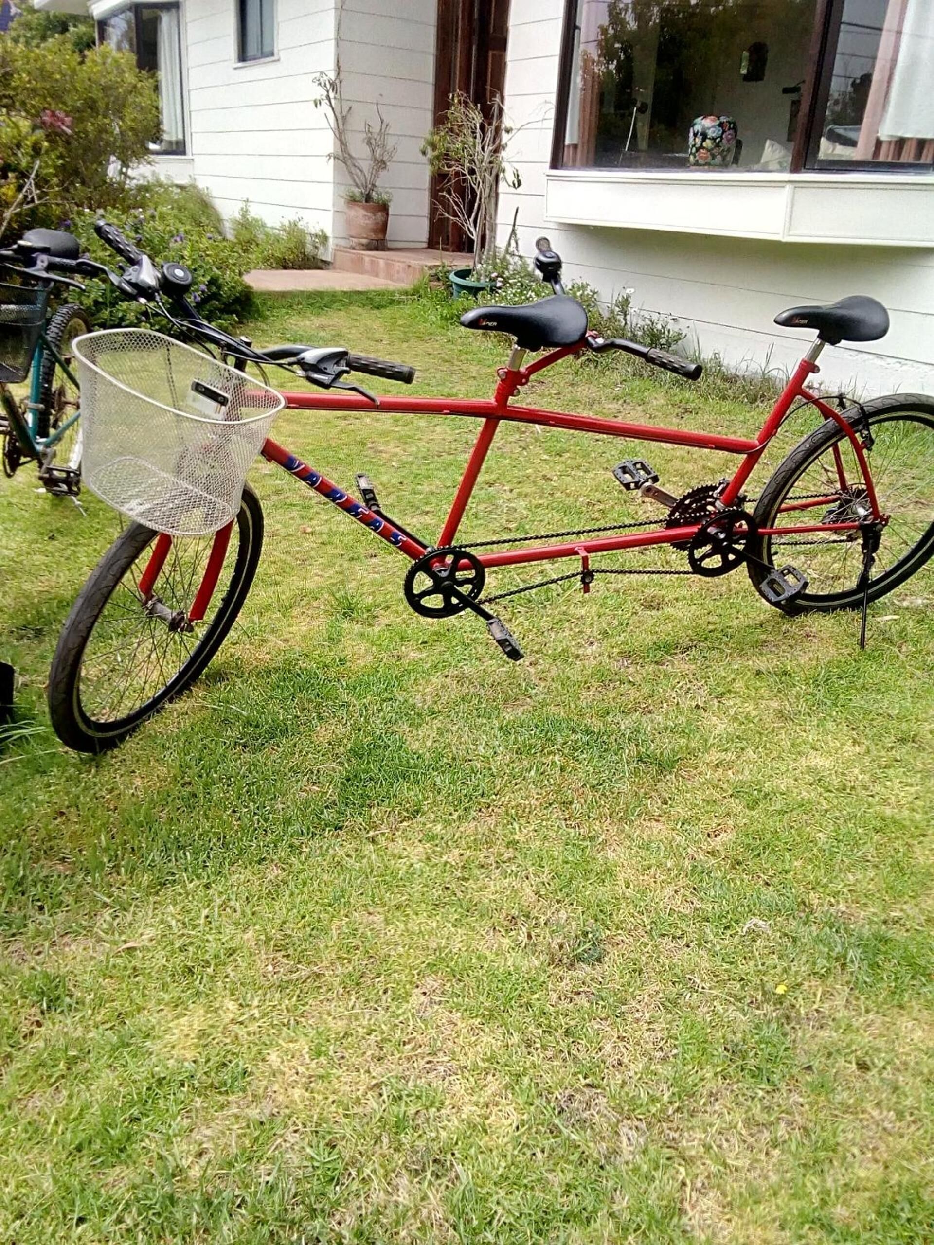 A red bicycle with a basket and pedals, parked on grass.