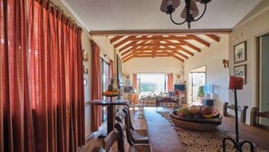 A spacious living area with a high ceiling, wooden beams, a dining table with chairs, and a fruit bowl. - B&B Rocas Santo Domingo (Santo Domingo)