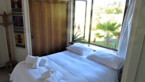 A neatly made bed with white linens and towels, a wooden door, and a window with a view of greenery outside. - B&B Rocas Santo Domingo (Santo Domingo)