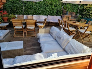 Un patio exterior con mobiliario de madera, incluyendo un sofá y sillas, y una mesa.