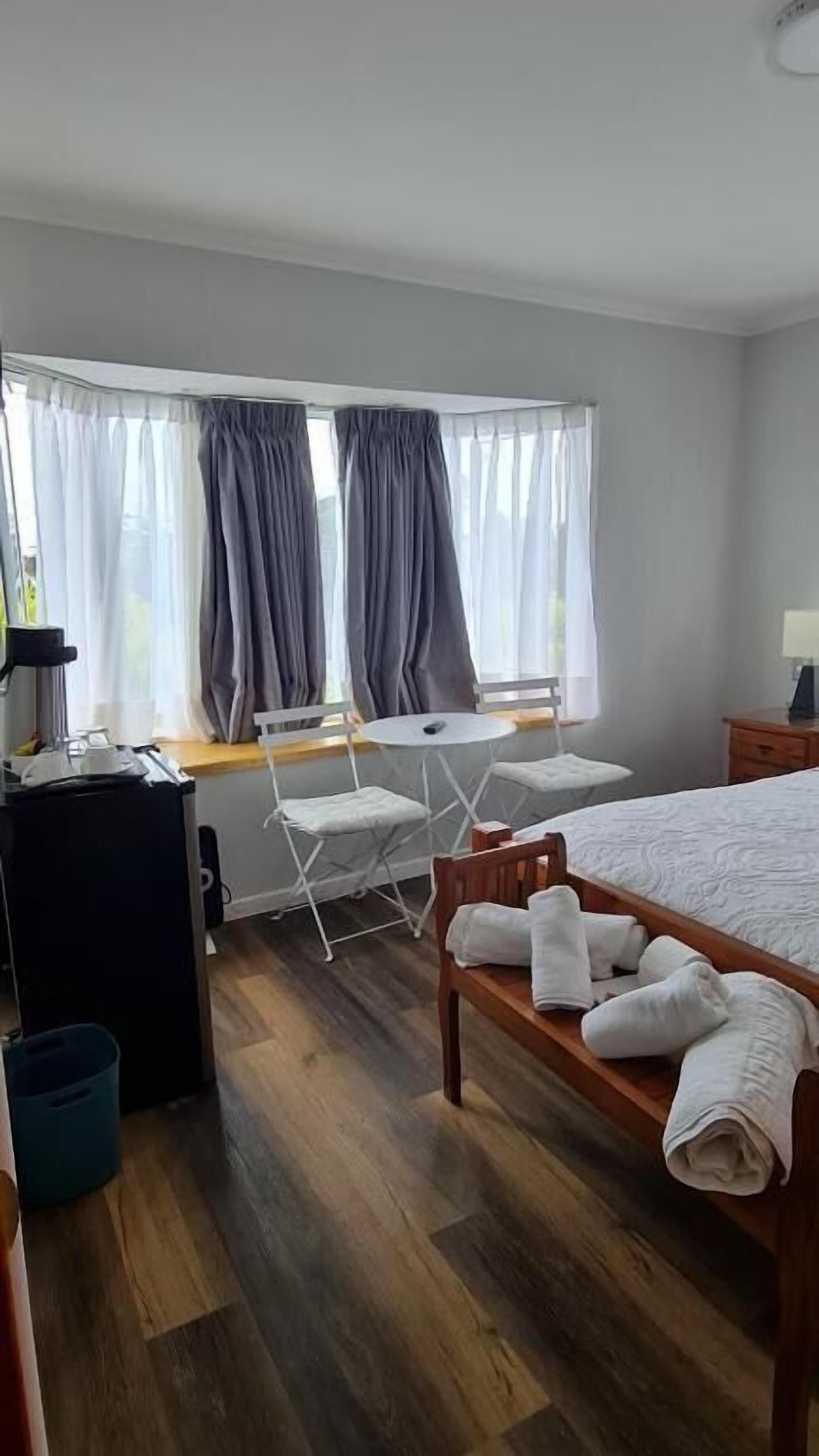 A hotel room with a bed, a desk, a chair, a table, and a window with curtains.