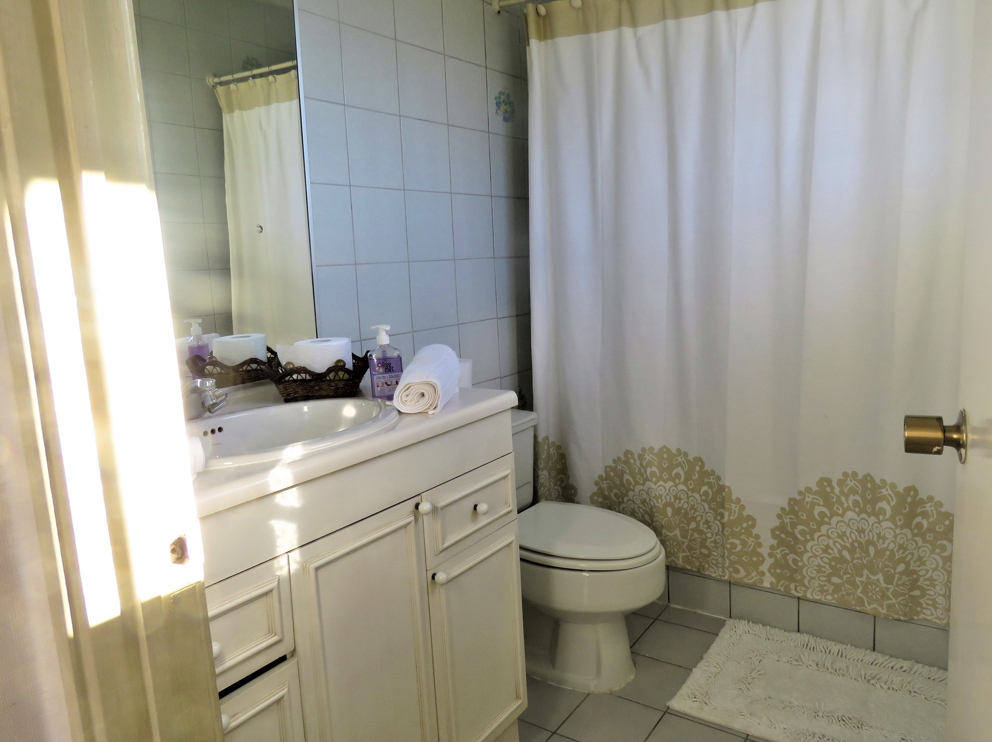 A bathroom with a white sink, toilet, and shower curtain. There are toiletries on the sink and a towel on the counter.