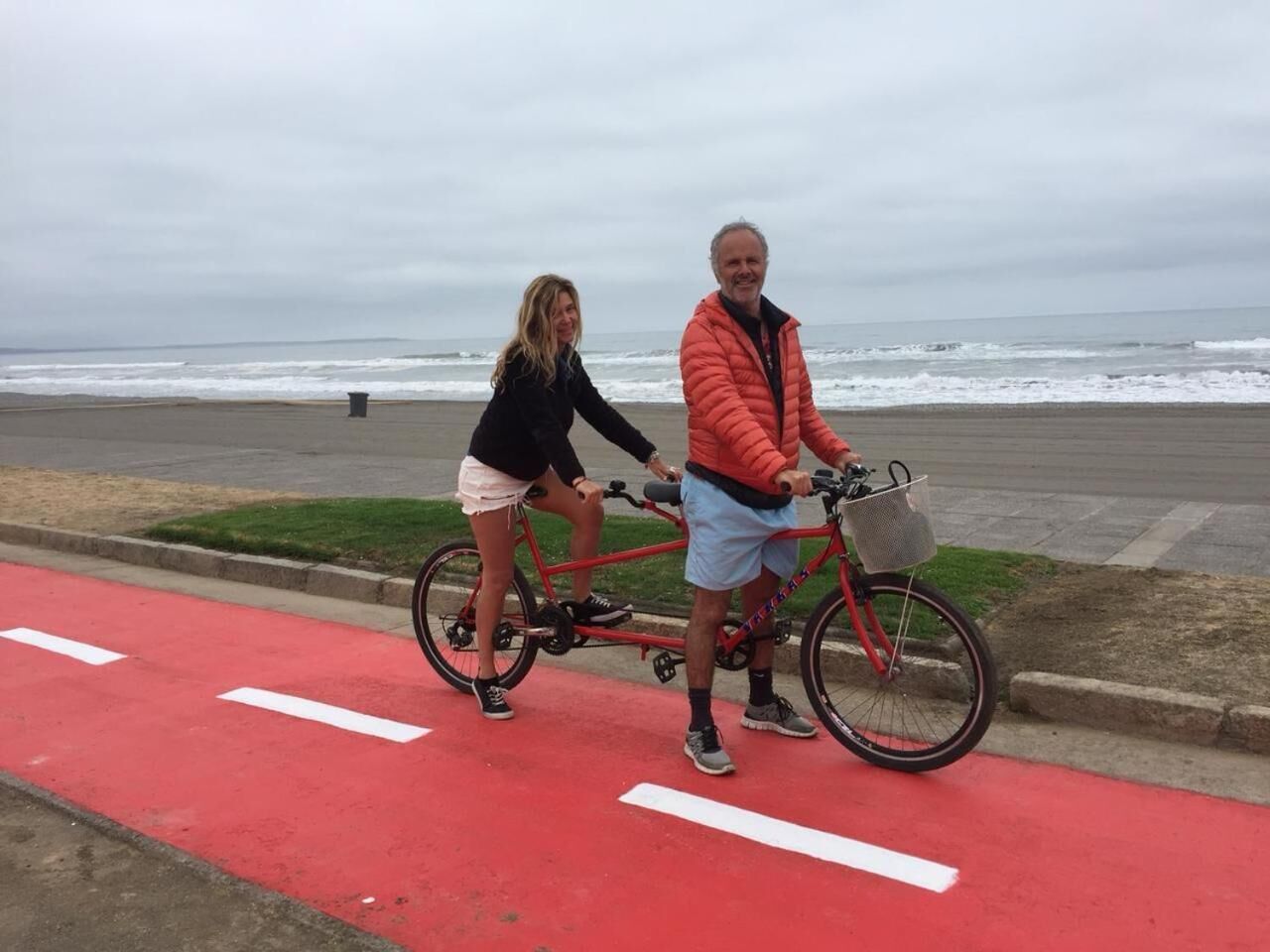 Two people on a red bike path near the beach with the ocean in the background.