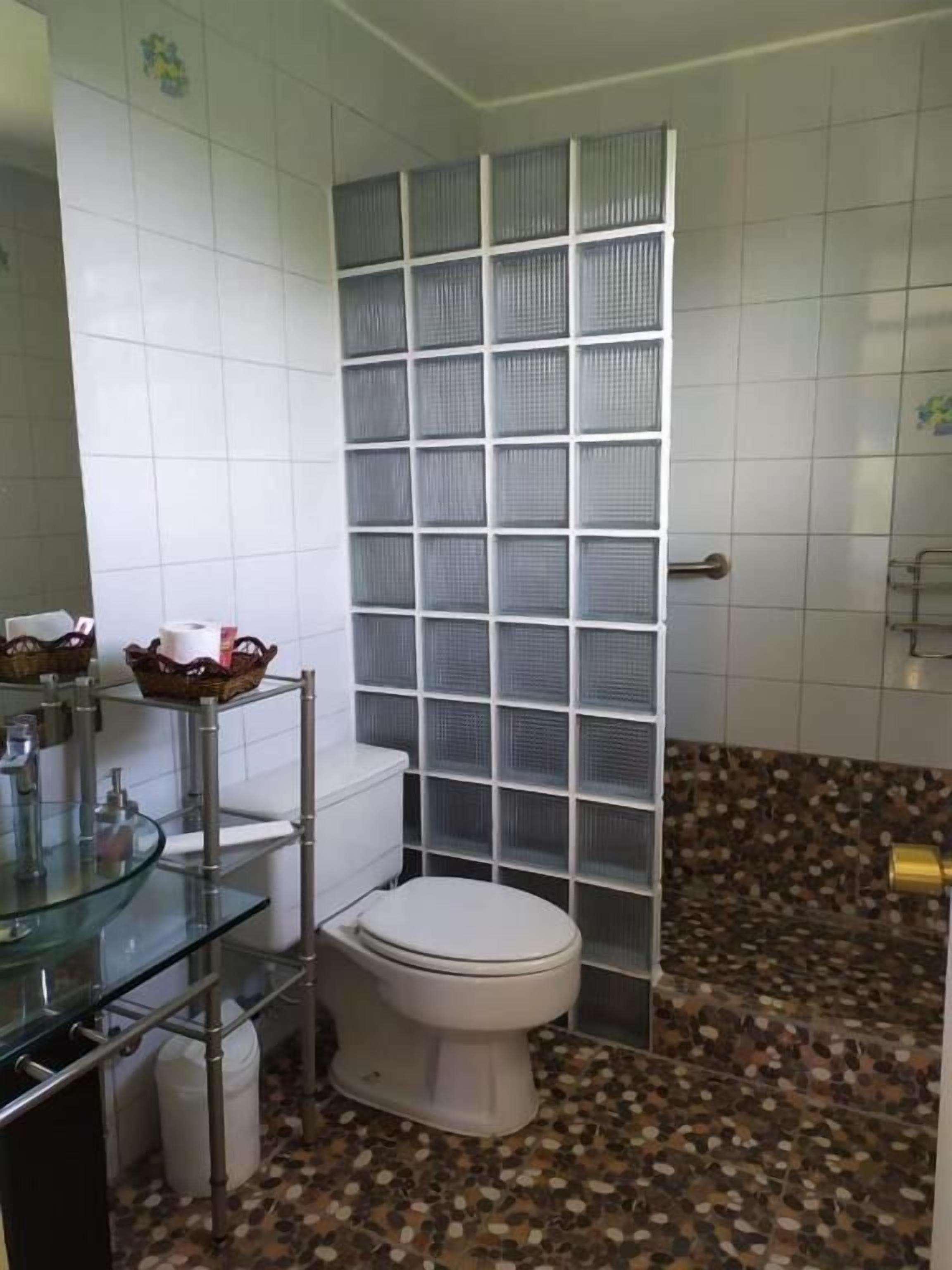 Un baño con inodoro blanco, lavabo de cristal y suelo de baldosas.